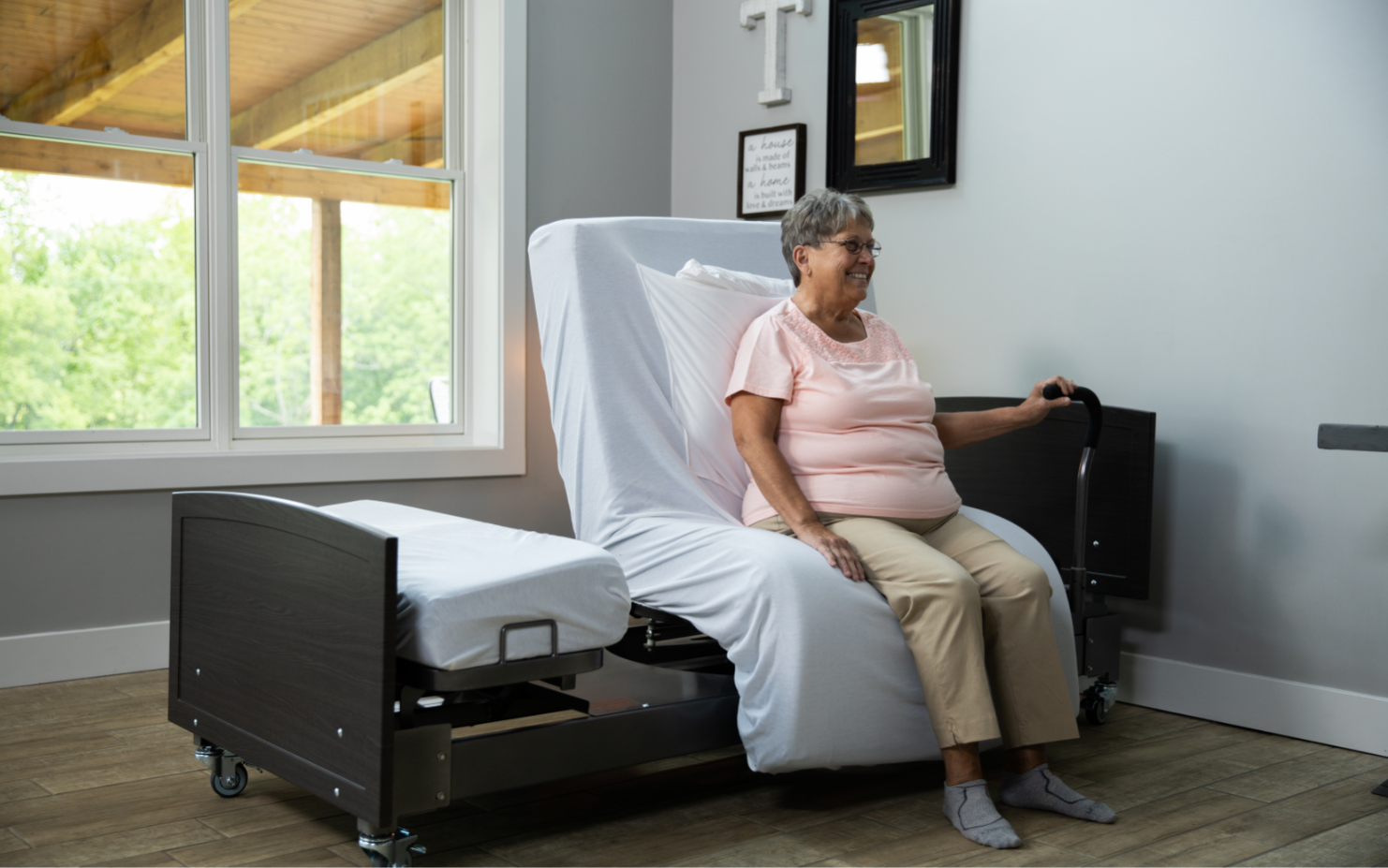 Image of the ActiveCare Fixed Height Hospital Bed mobility bar and woman sitting on hospital bed.