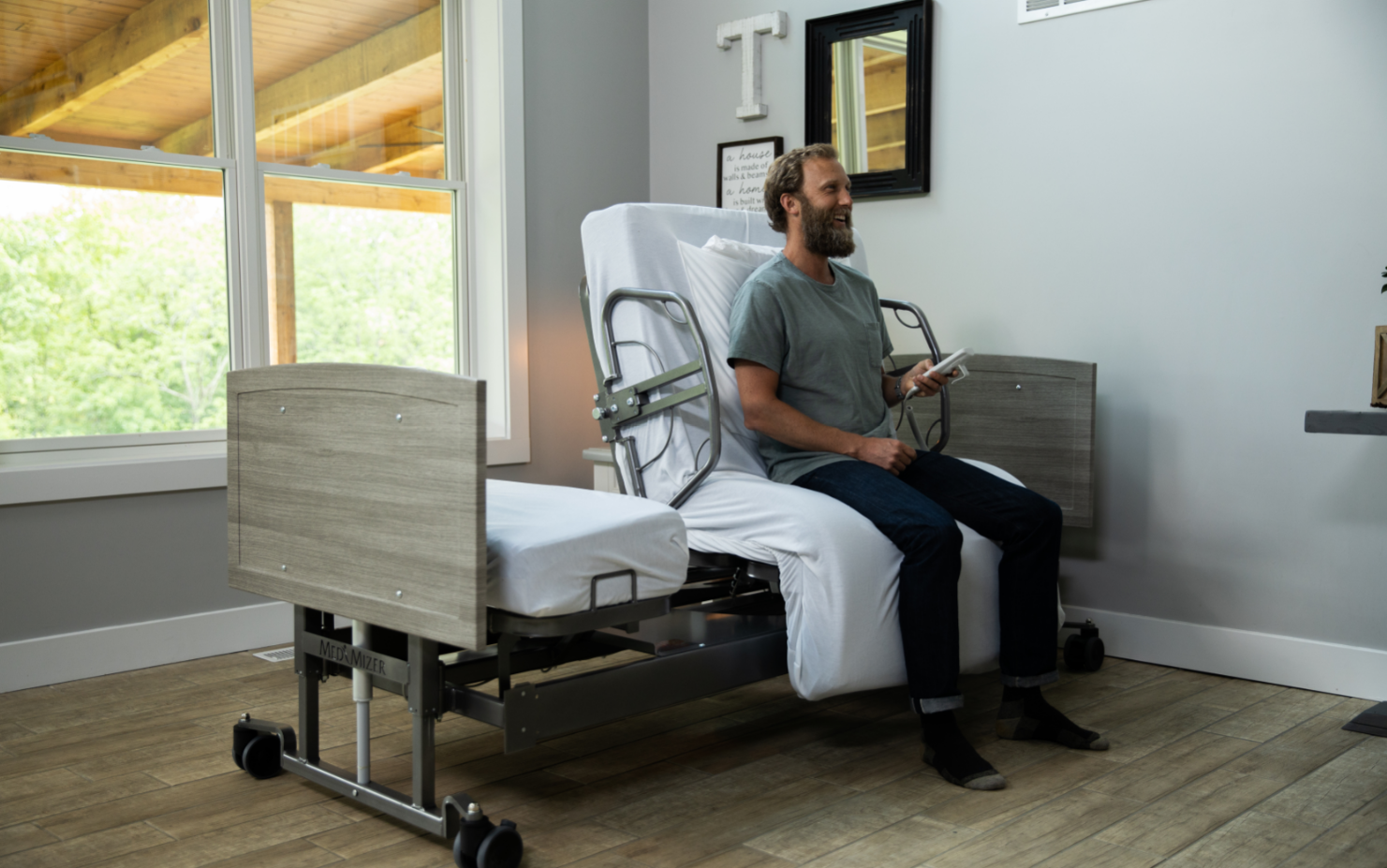 ActiveCare Standard Hospital Bed 4 Image of man sitting in bedroom on the ActiveCare hospital bed that's rotated.