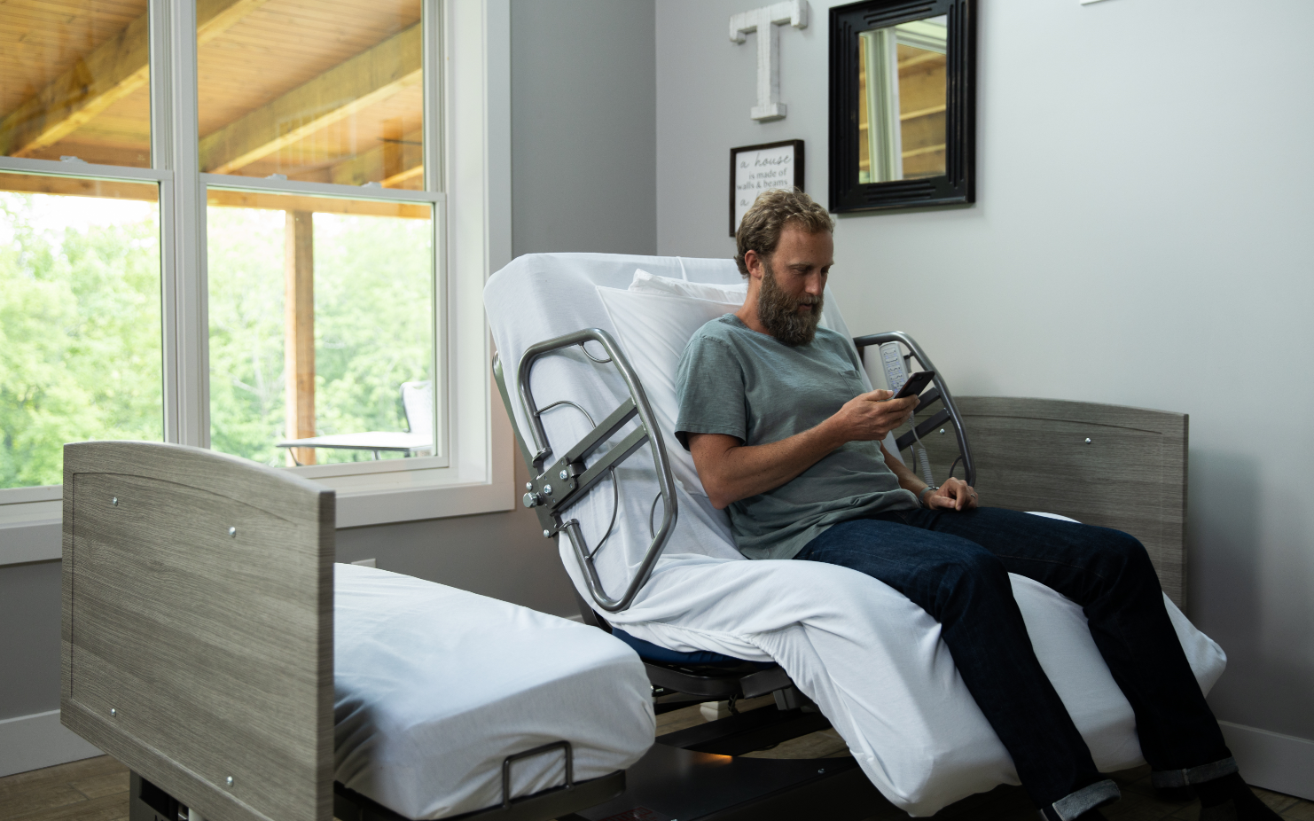Image of man sitting in ActiveCare hospital bed and using his phone.