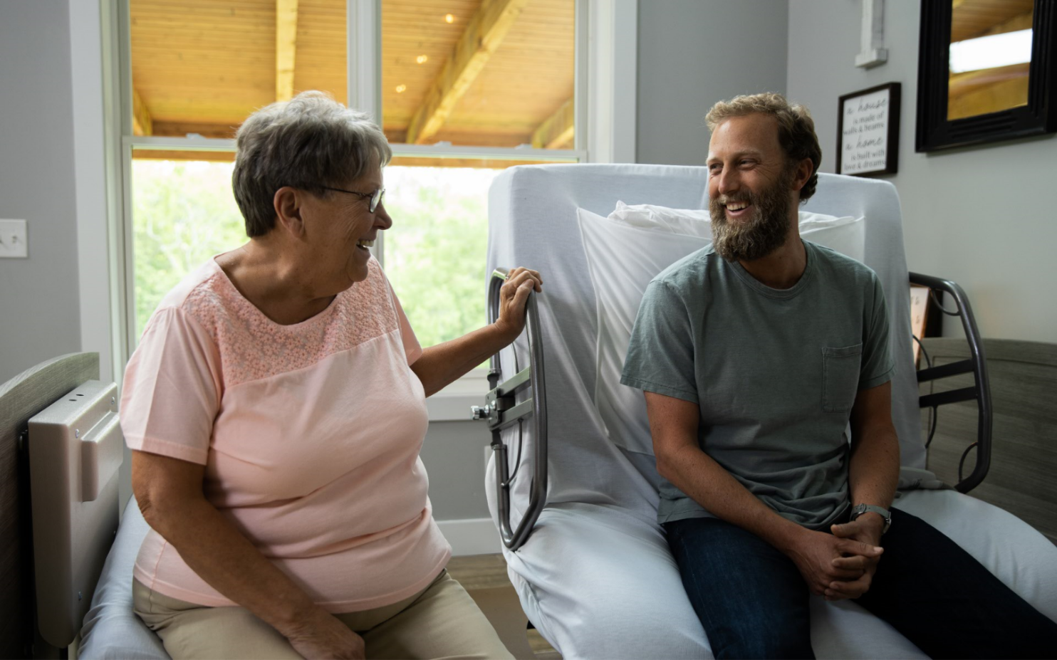 ActiveCare Standard Hospital Bed 6 Image of man and woman sitting on the ActiveCare hospital bed chatting.