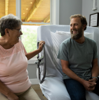 ActiveCare Standard Hospital Bed 6 thumbnail Image of man and woman sitting on the ActiveCare hospital bed chatting. thumbnail