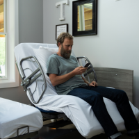 ActiveCare Standard Hospital Bed 5 thumbnail Image of man sitting in ActiveCare hospital bed and using his phone. thumbnail