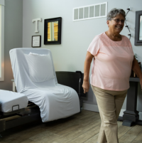 Image of the ActiveCare Fixed Height Bed and woman walking away from it. thumbnail