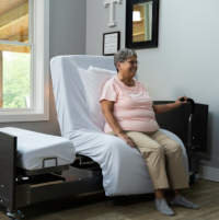 Image of the ActiveCare Fixed Height Hospital Bed mobility bar and woman sitting on hospital bed. thumbnail