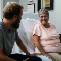 Image of woman and man chatting while sitting on ActiveCare Hospital Bed. thumbnail