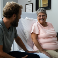 ActiveCare Fixed Height Hospital Bed 5 thumbnail Image of woman and man chatting while sitting on ActiveCare Hospital Bed. thumbnail