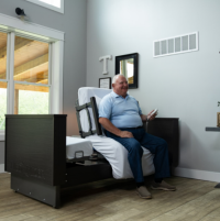 Image of ActiveCare Deluxe Hospital Bed with man sitting down on it. thumbnail
